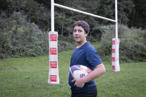 jeune avec un ballon de rugby sous le bras sur le terrain