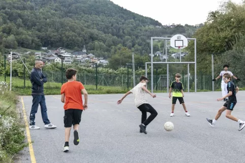Un groupe de jeunes en train de jourer au foot dehors avec un éducateur